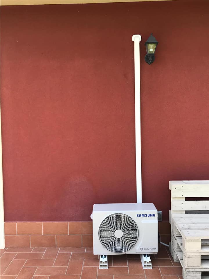 Muro rosso con unità esterna di condizionamento dell'aria, tubo bianco e lampada da veranda accanto a pallet impilati.