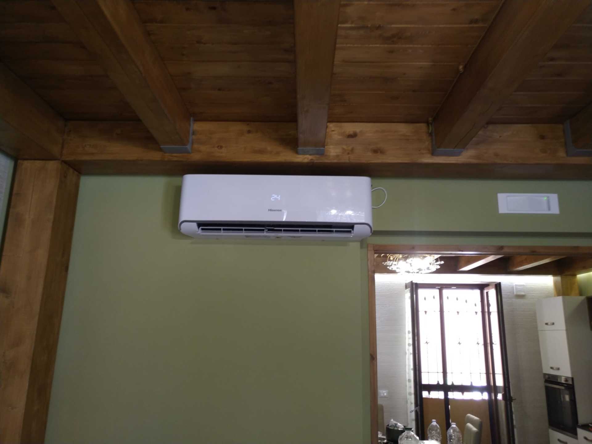 Condizionatore d'aria a parete su una parete verde sotto un soffitto in legno, sopra una porta e una finestra in una stanza