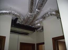 Soffitto con condotti isolati in argento e bocchetta di ventilazione a parete in un corridoio interno.