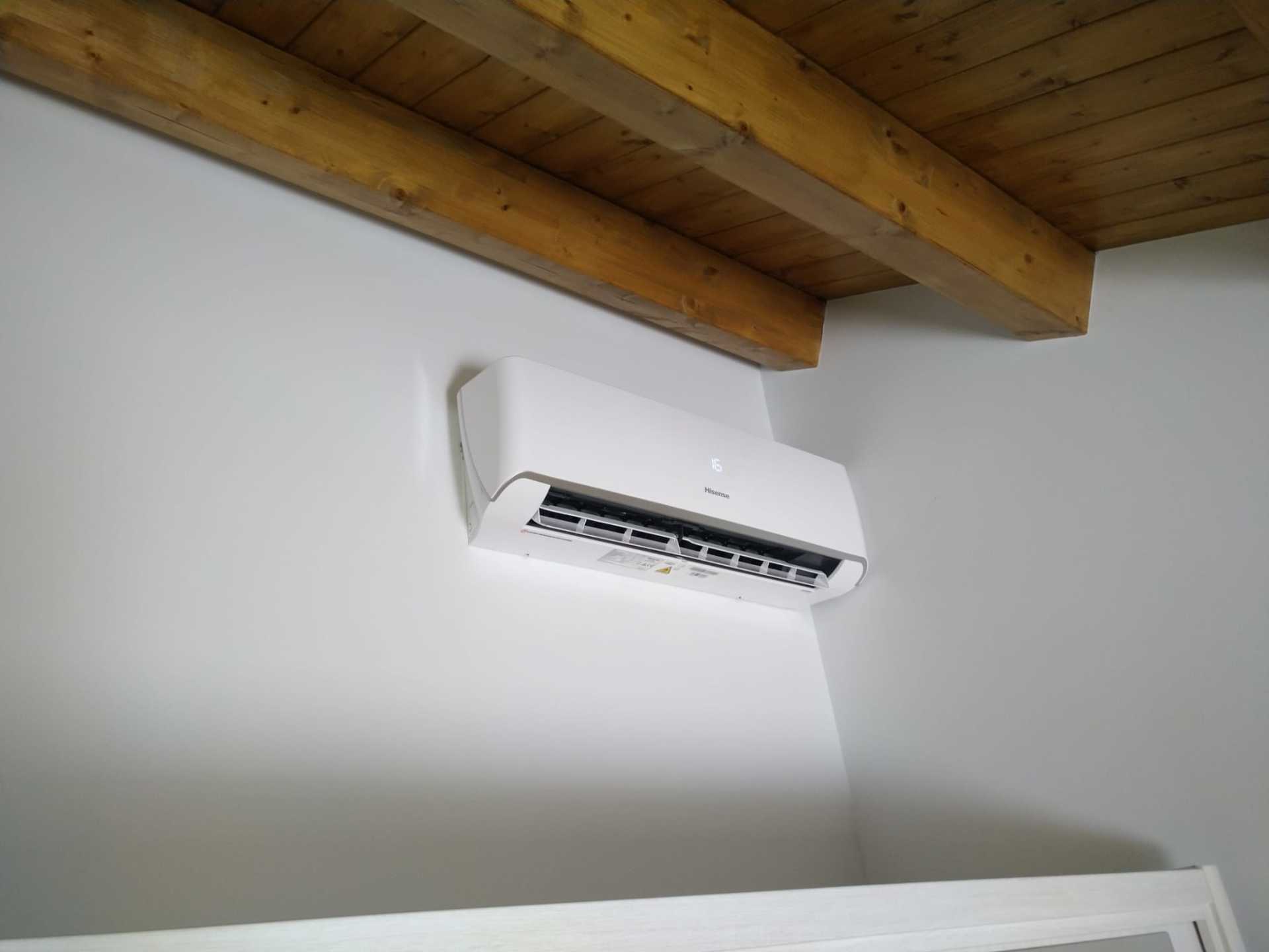 Parete bianca con condizionatore d'aria montato sotto le travi di legno a vista del soffitto.