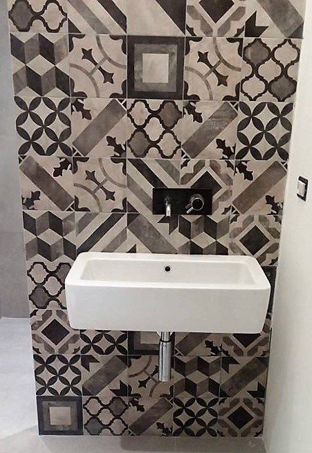 Piccolo lavabo bianco a parete su una parete del bagno rivestita di piastrelle decorate, con specchio e rubinetto.