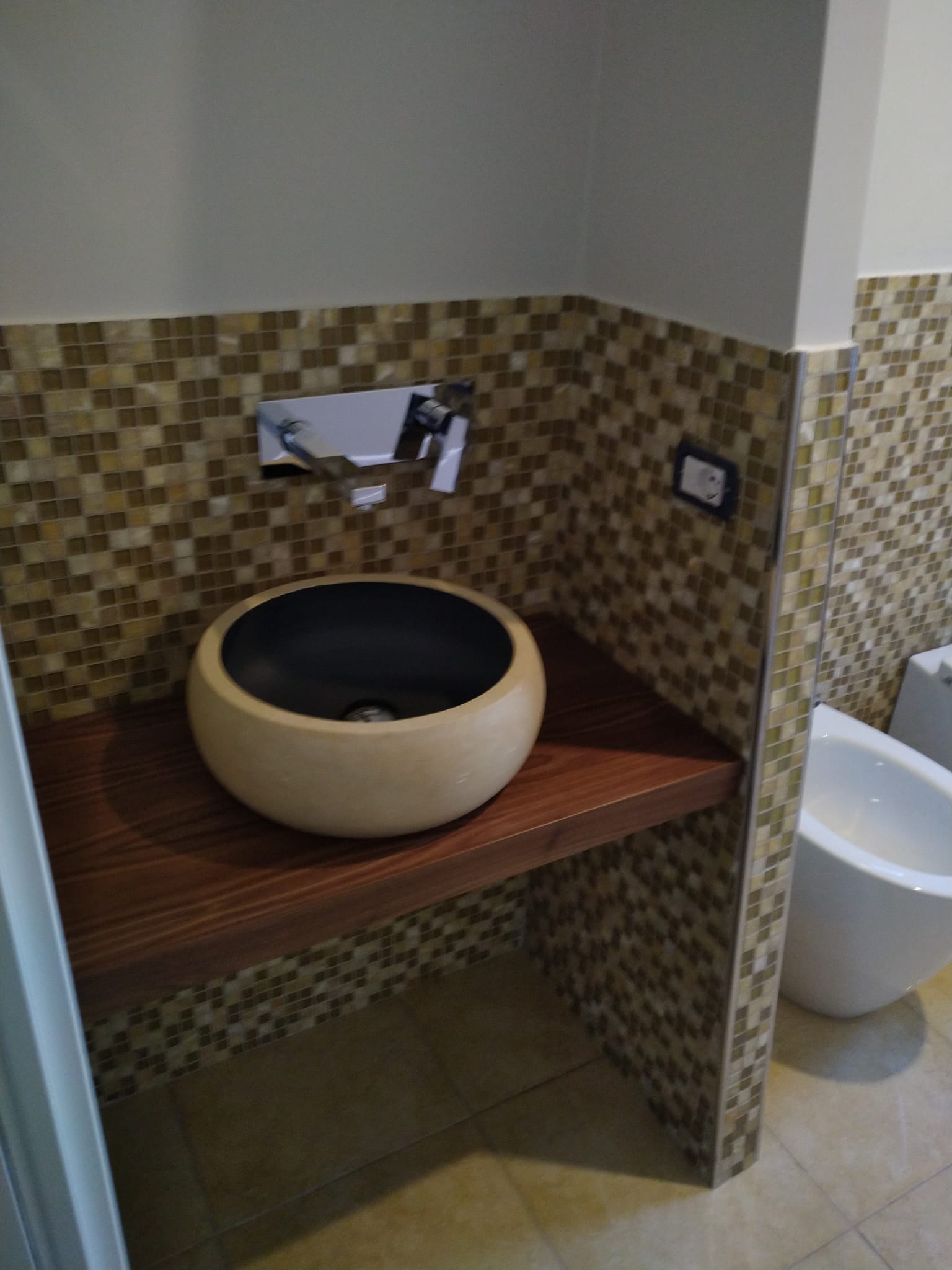 Angolo lavabo moderno in bagno con lavabo rotondo beige, pareti rivestite con piastrelle a mosaico e WC nelle vicinanze.