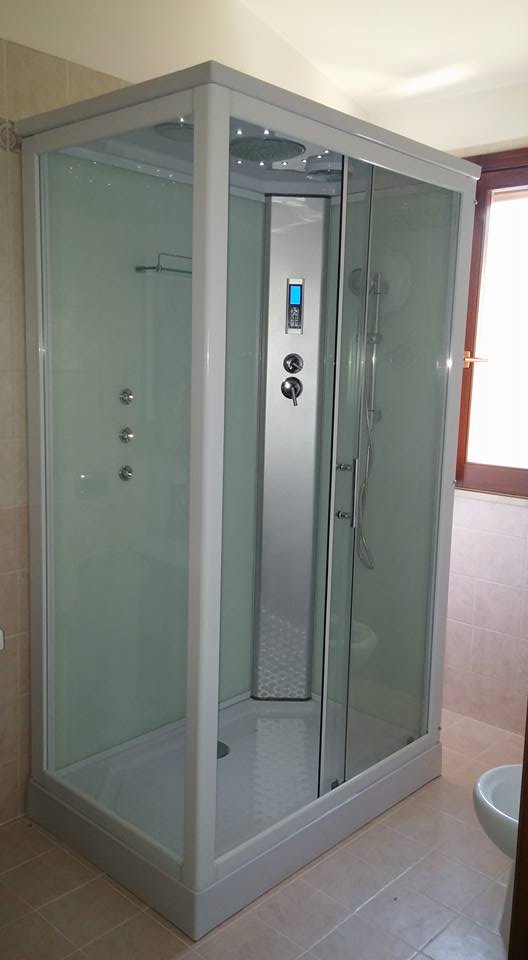 Box doccia in vetro con rubinetteria cromata in un bagno piastrellato.