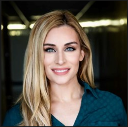 A blonde woman wearing a blue shirt smiles for the camera