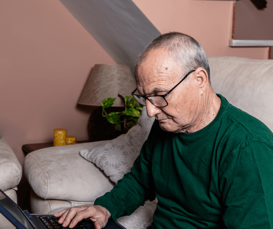 Man in green sweater using a laptop on a couch in a living room