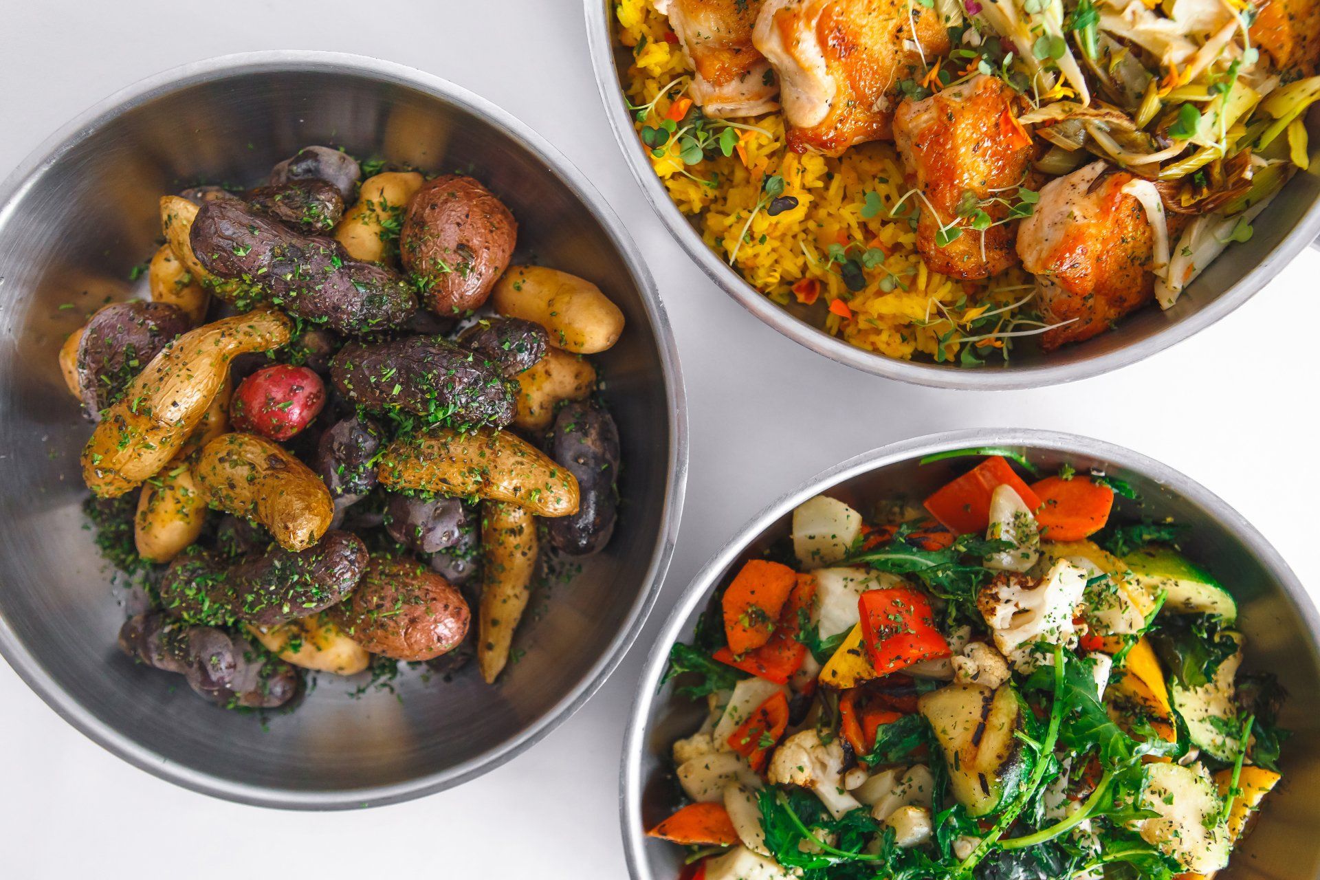 skillets filled with chicken, rice, potatoes, and vegetables on a white tablecloth. 