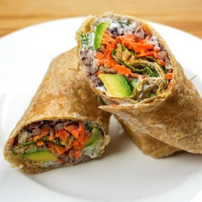 Burrito cut in half on a white plate, filled with carrots, avocado, and rice.