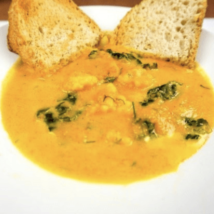 Bowl of orange soup with green vegetables and toasted bread.