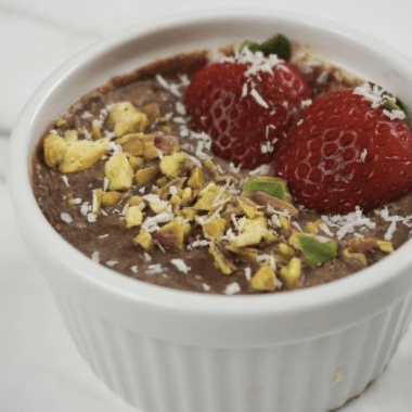 Chocolate mousse dessert with strawberries, pistachios, and coconut flakes in a white ramekin.