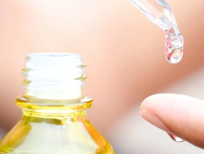 Dropper dispensing liquid from a bottle onto a finger. Light background.