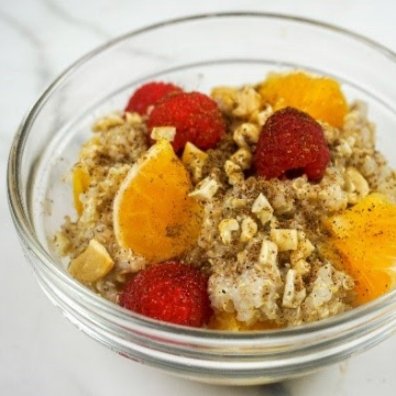 Oatmeal in glass bowl topped with raspberries, orange slices, and chopped nuts.