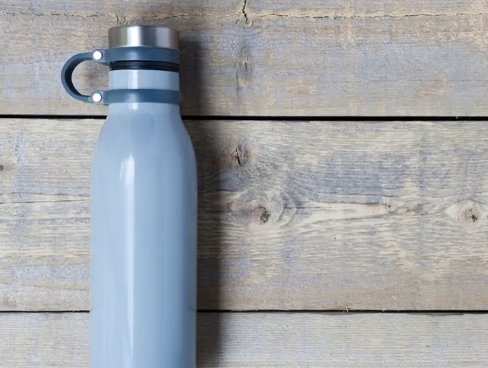 Light blue water bottle with silver lid and black handle on wooden planks.