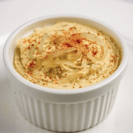 Creamy hummus topped with onions and paprika in a white ramekin.