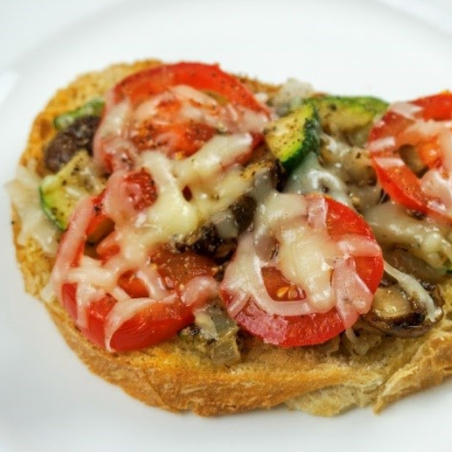 Toasted bread topped with melted cheese, tomato slices, zucchini, and mushrooms.
