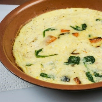Frittata with spinach and orange vegetables in a copper-colored pan.