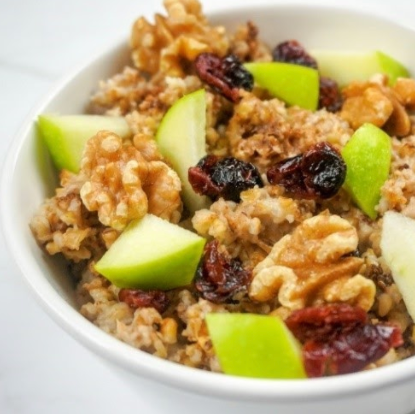 Bowl of oatmeal with green apple slices, walnuts, and dried cranberries.
