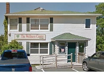 The Wellness Centre building with green roof and sign, blue truck and gray car parked in front.