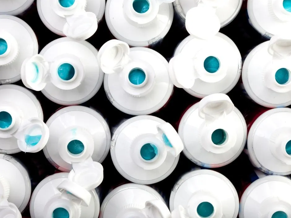 Close-up of white toothpaste tubes with open caps, showing blue toothpaste.