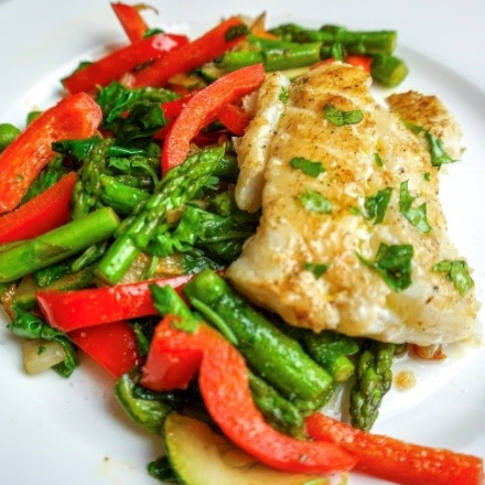 White plate with sautéed fish, red peppers, and asparagus.