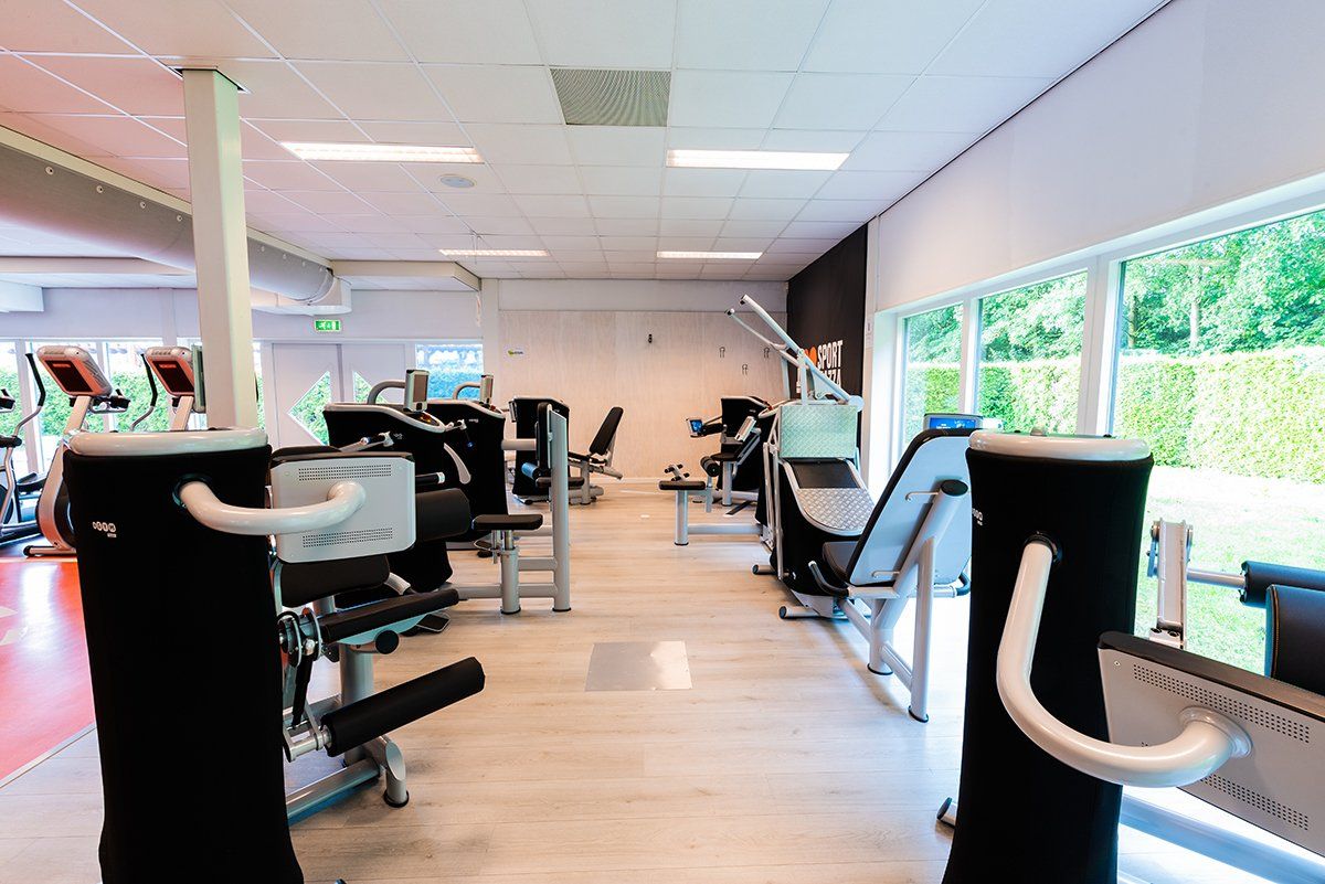Een sportschool met veel fitnessapparatuur en veel ramen.