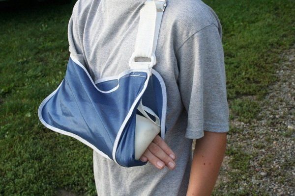 A young boy with a broken arm is wearing a blue arm sling.
