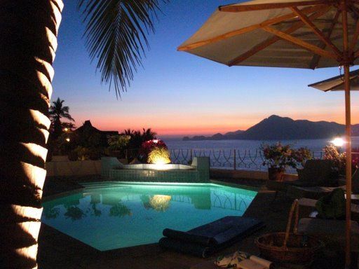 a swimming pool is lit up at night with an umbrella in the foreground