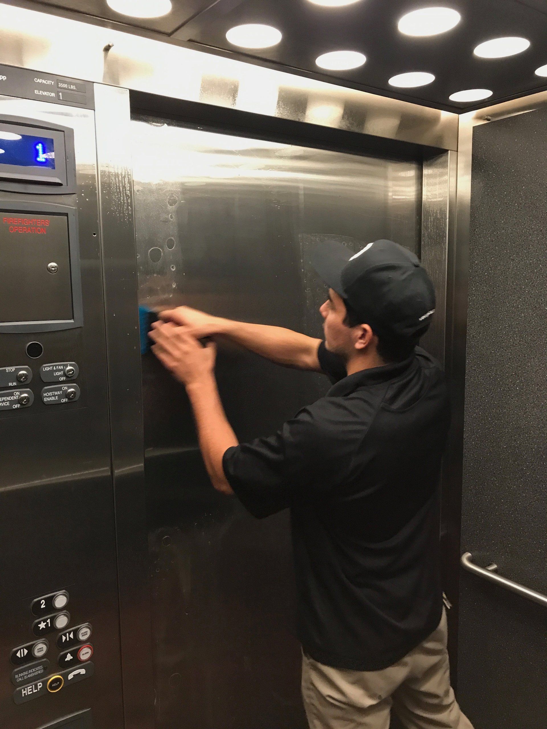Man in black shirt cleaning a stainless steel elevator control panel with a cloth