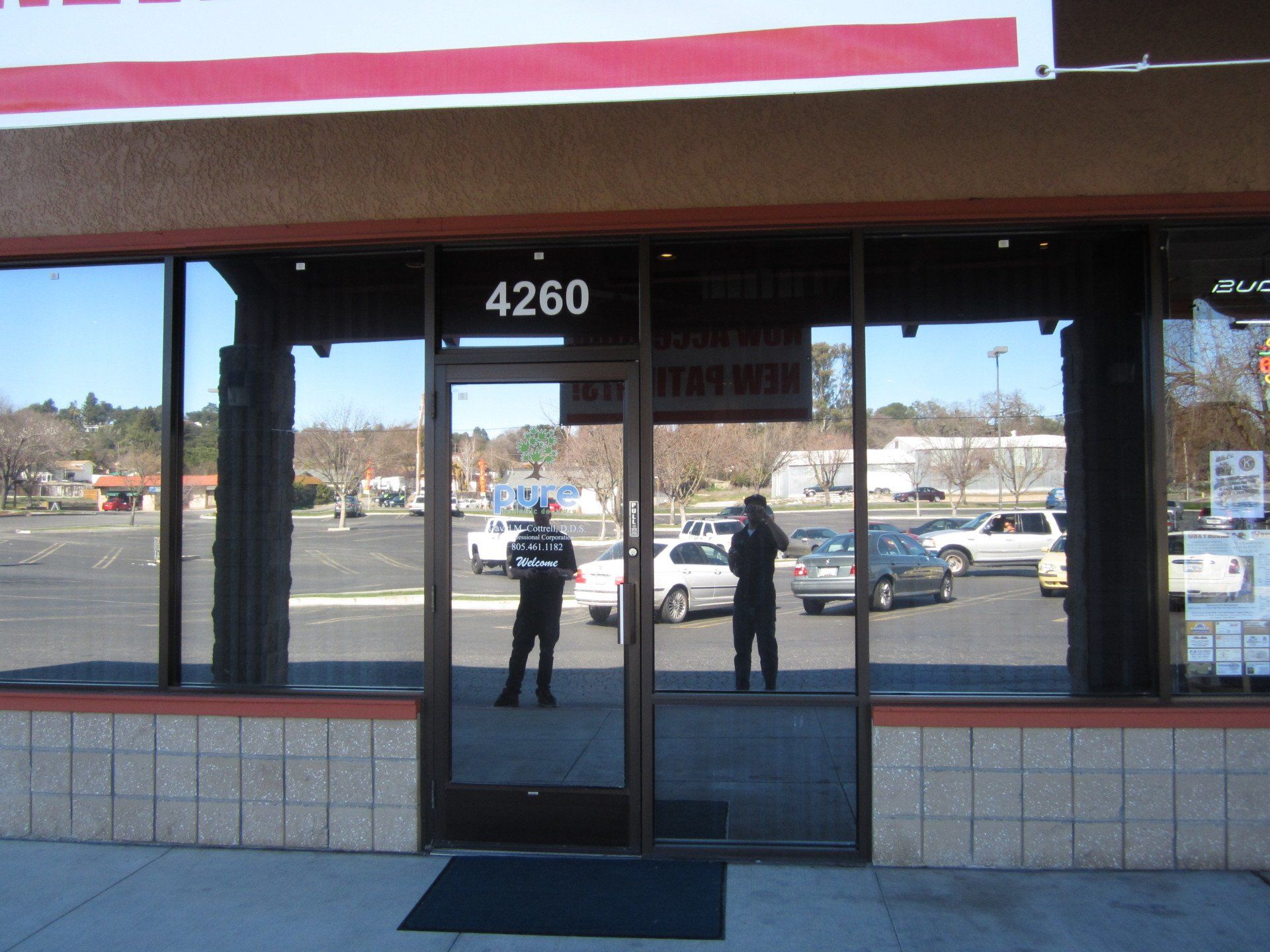 Storefront entrance with glass doors and the number 4260 above, reflecting two people outside.
