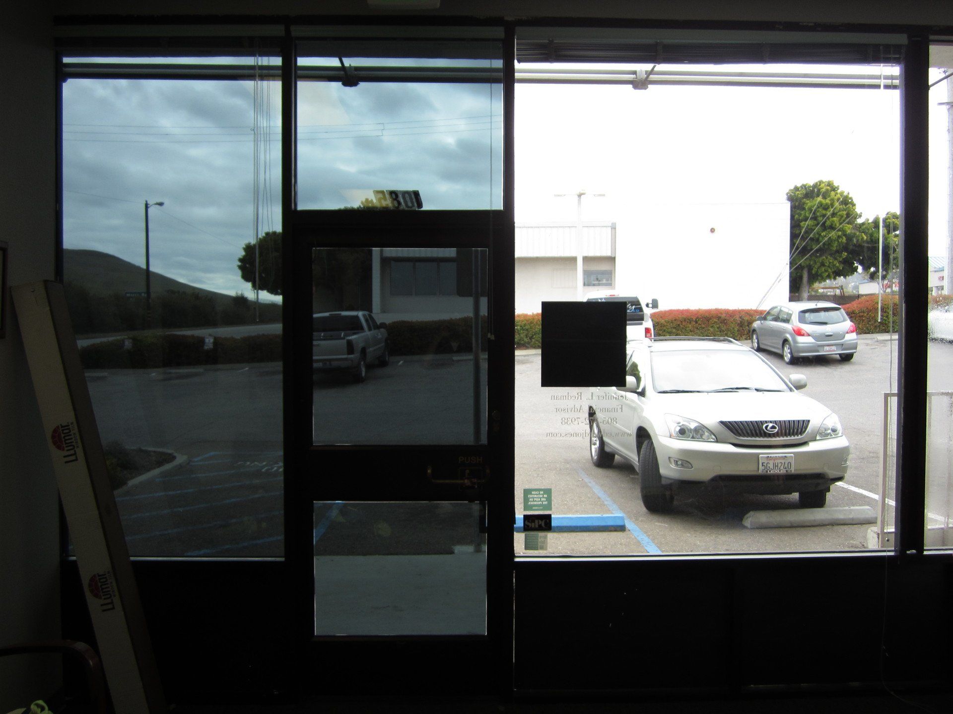 View through glass doors to a parking lot with a white SUV and a gray car outside.