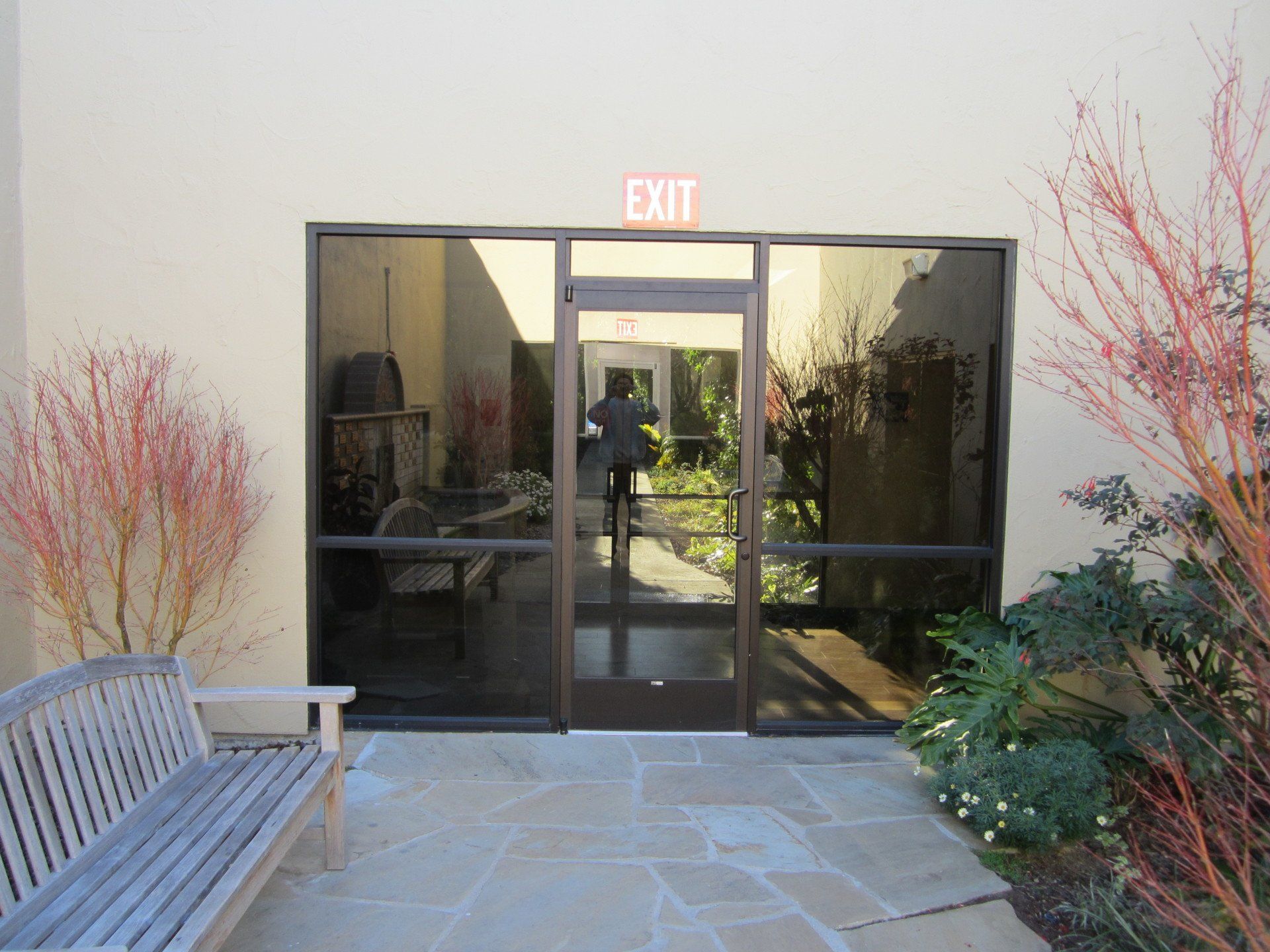 Glass exit doors at a building entrance with an illuminated exit sign and benches outside