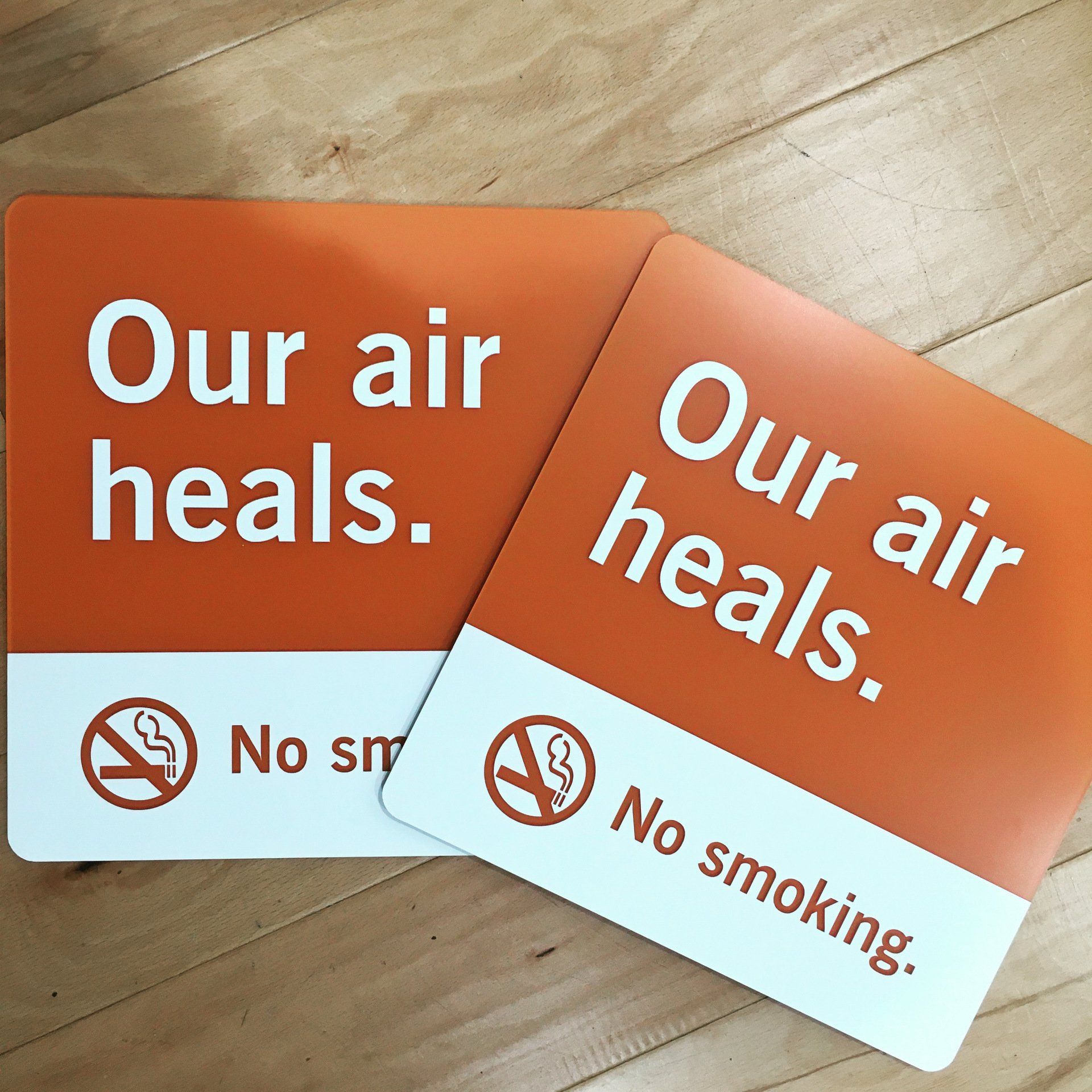 Two orange and white no-smoking signs reading “Our air heals.” on a wooden surface