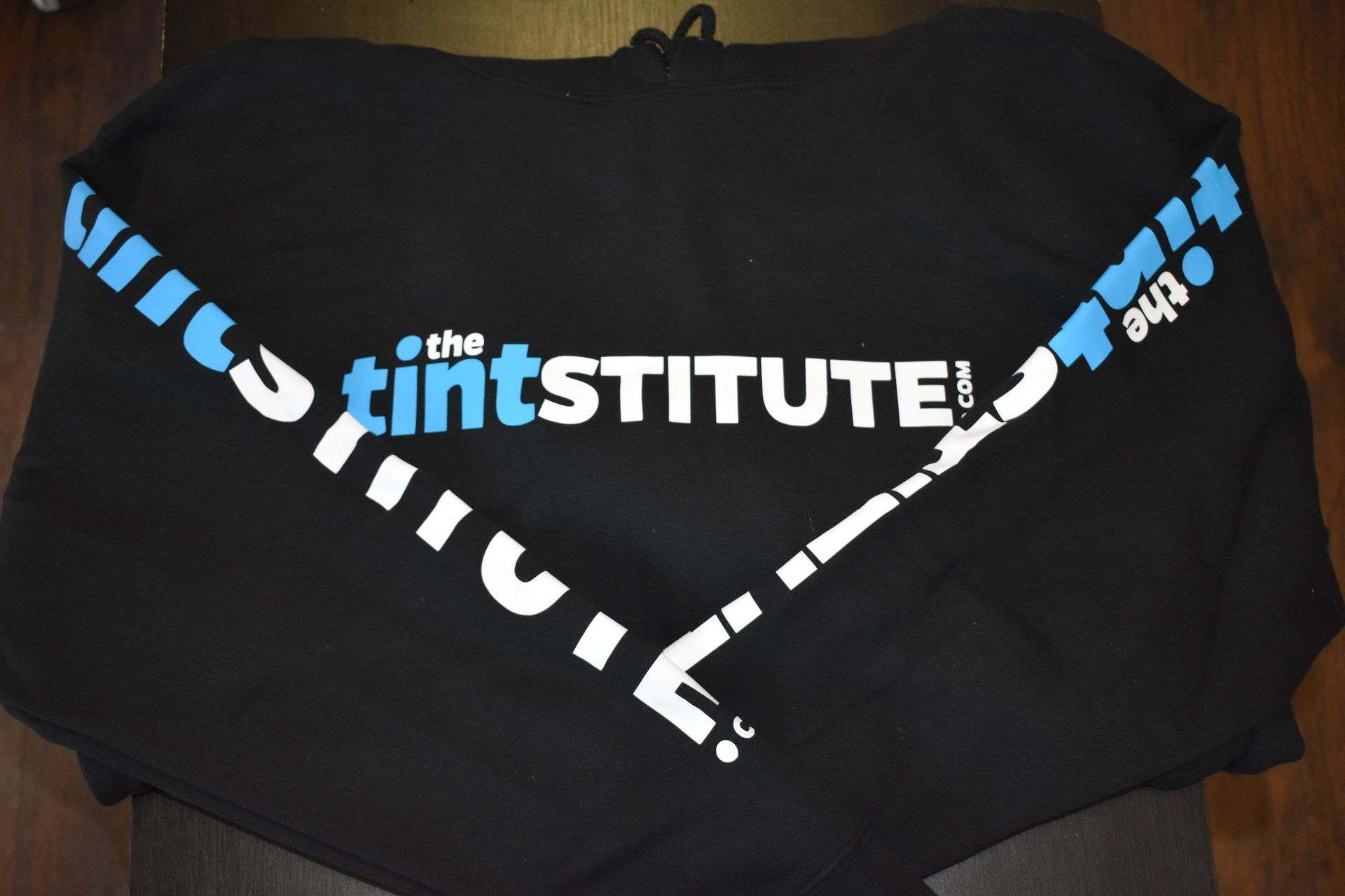 Black T-shirt with the white and blue “the tintSTITUTE” logo printed diagonally across the chest.