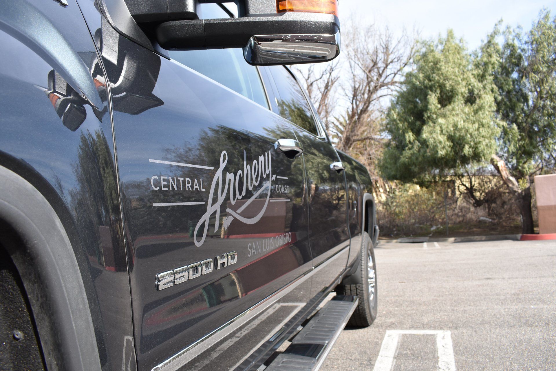 Black SUV parked in a lot, side view with chrome logo and running board under bright daylight