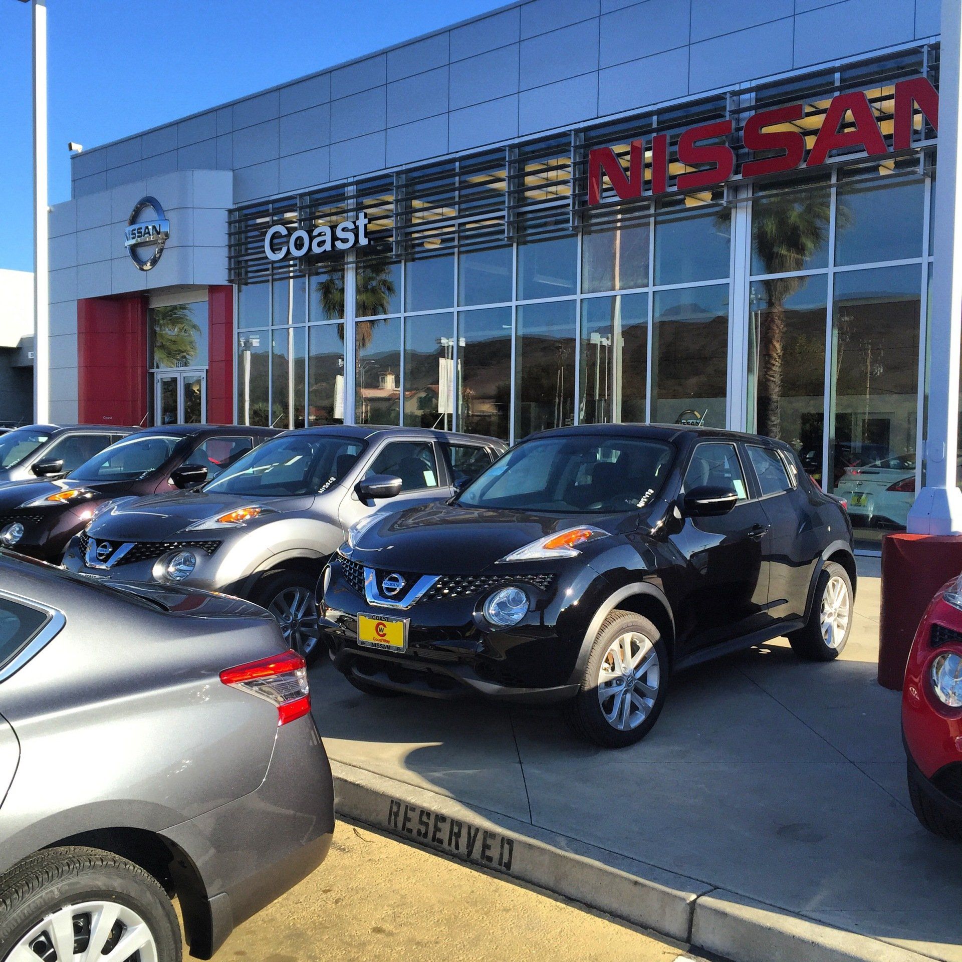 Nissan dealership exterior with rows of parked cars under a clear blue sky