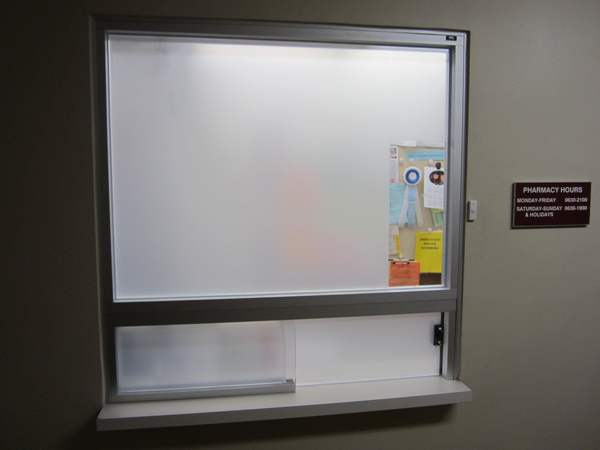 Small service window with frosted glass, a pass-through shelf, and a posted notice on the right wall.