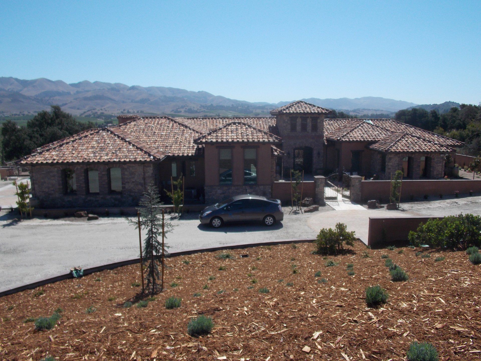 Single-story stucco house with red tile roof, parked car, and desert mountains in the background.