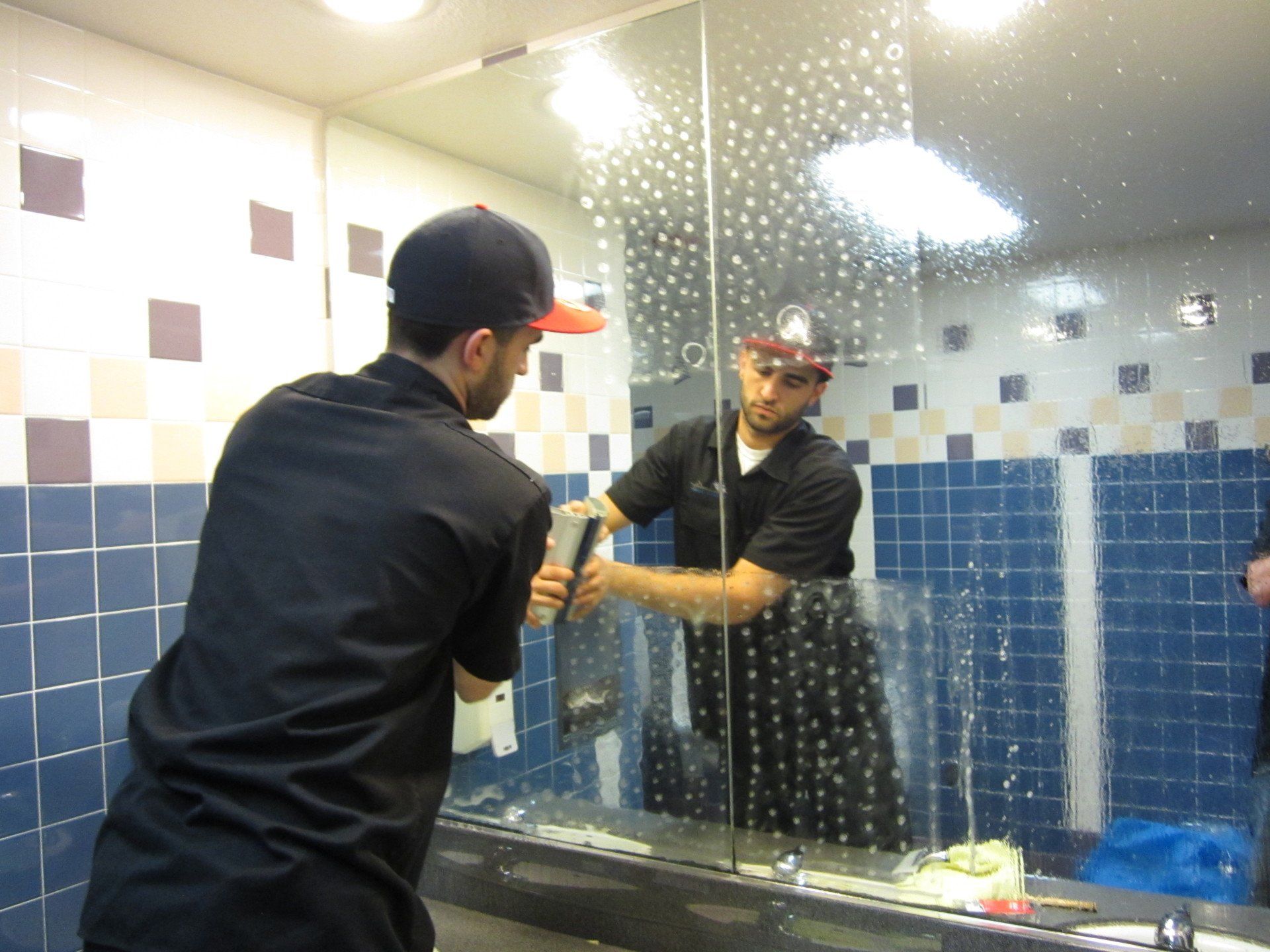 Person cleaning a tiled bathroom mirror with a squeegee, reflected in the glass.