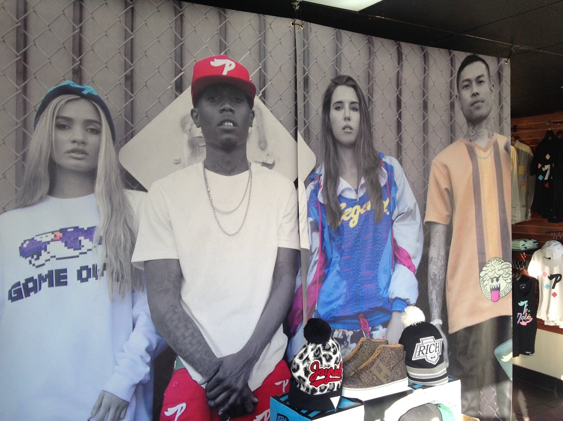 Four people standing behind display tables with shoes and hats in a market stall