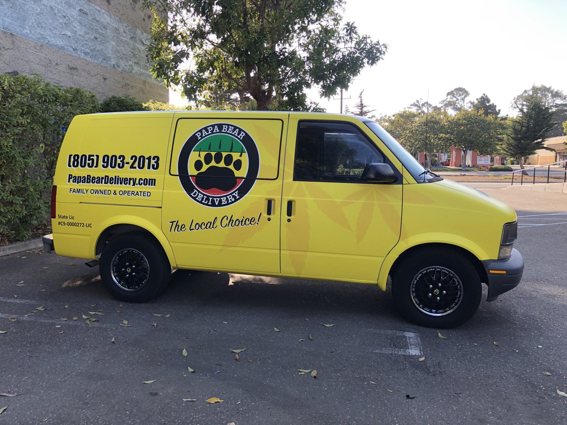 Yellow delivery van with company logo and contact number parked outdoors on a street.