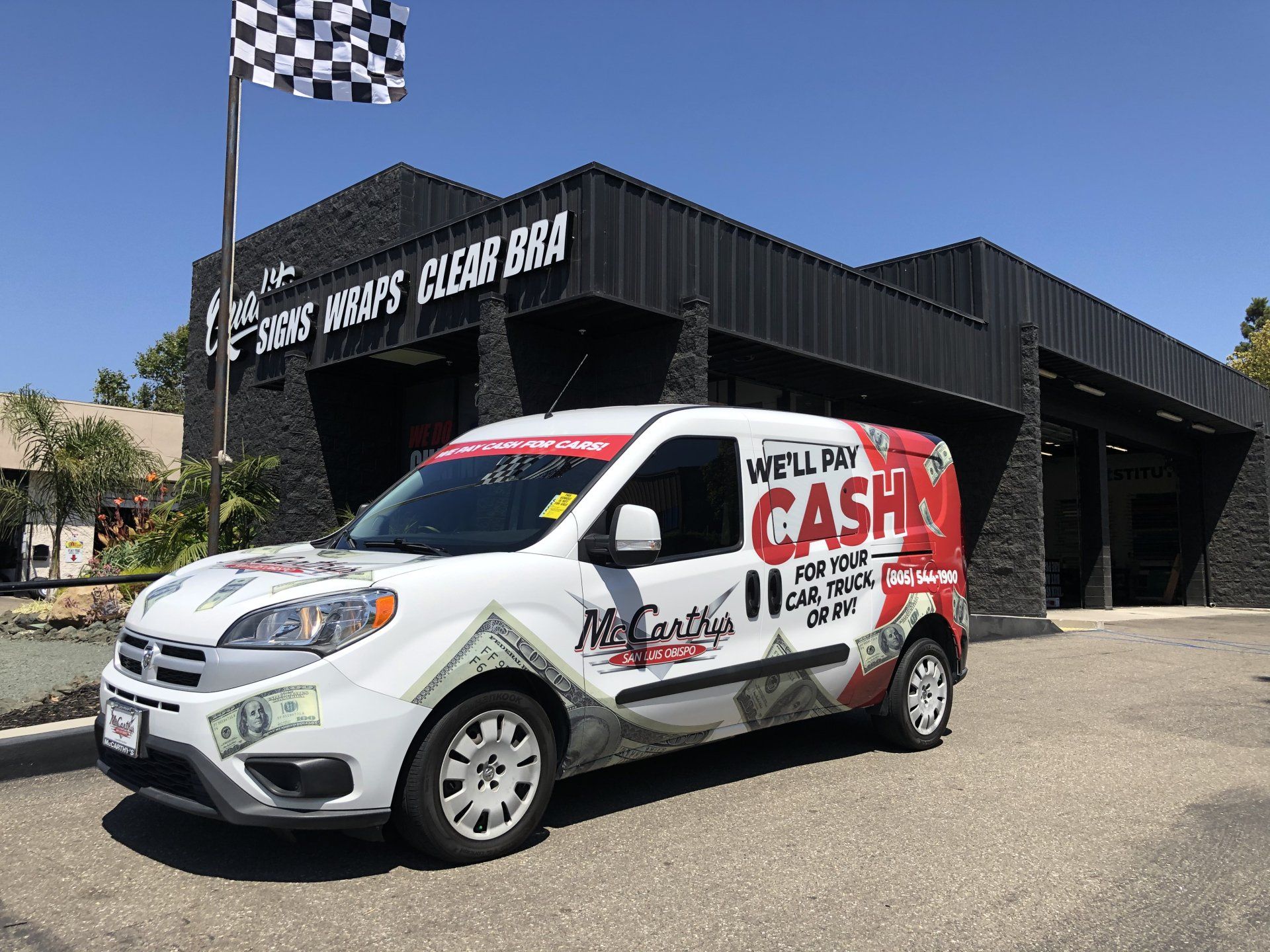 White cash-for-cars van parked outside a black shop with a checkered flag sign.