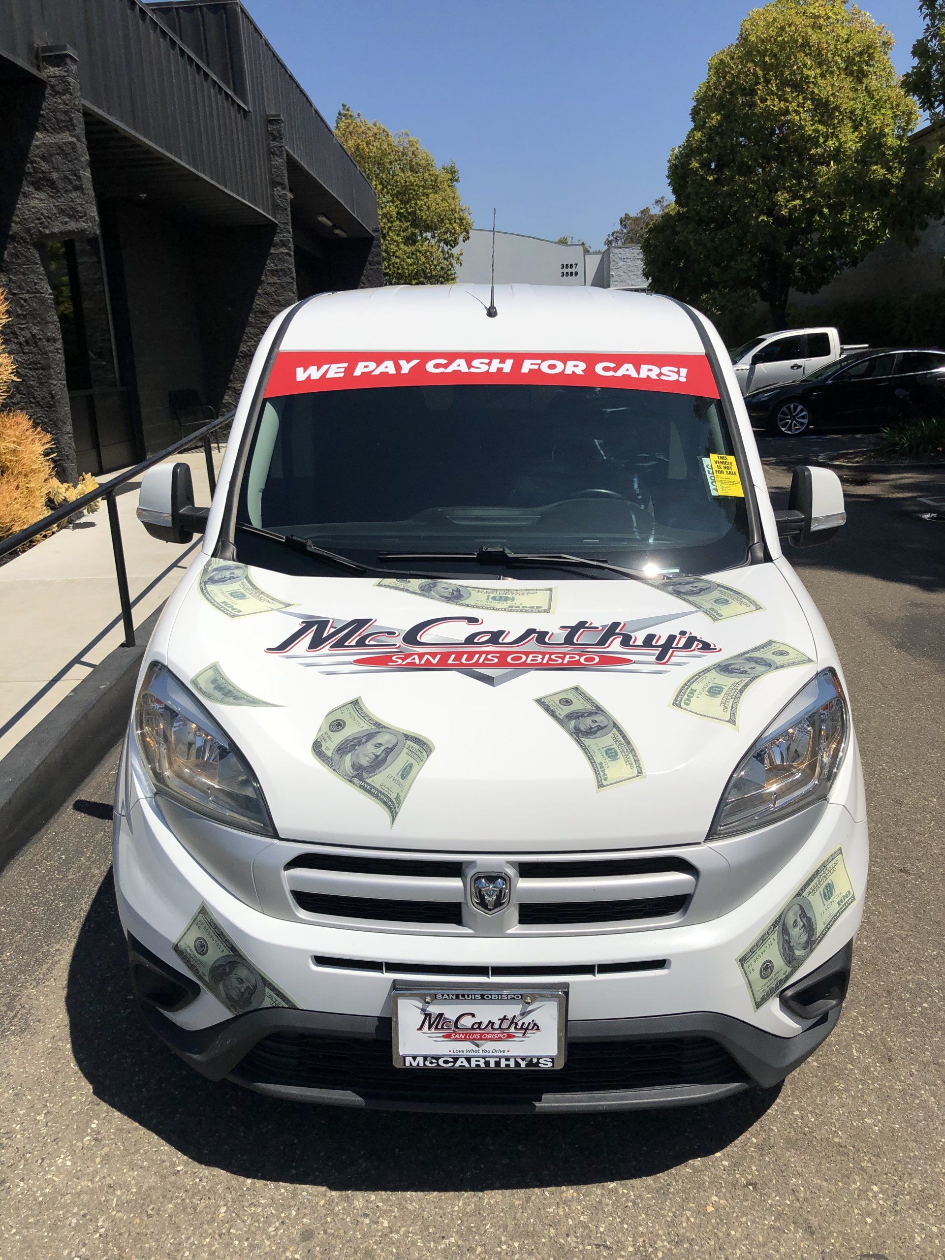 White pickup truck with red “WE PAY CASH FOR CARS” banner and money graphics parked on a street