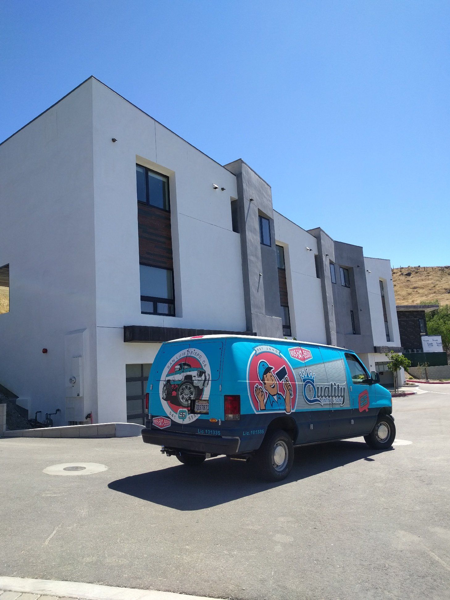 Blue delivery van parked outside a modern white building under a clear sky