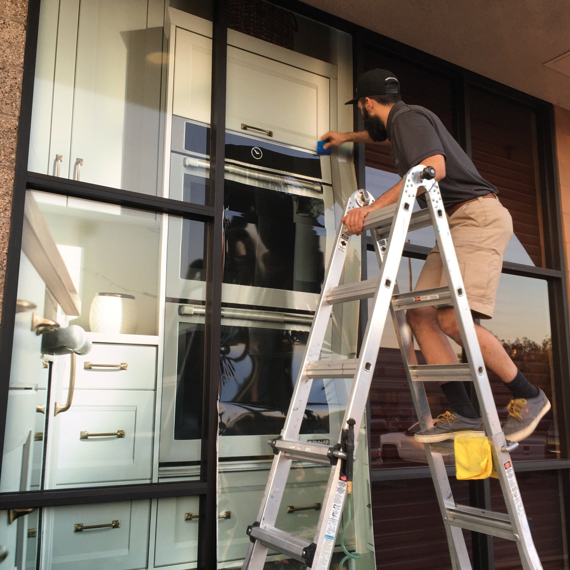 Worker on a ladder installing window film on a glass storefront facade