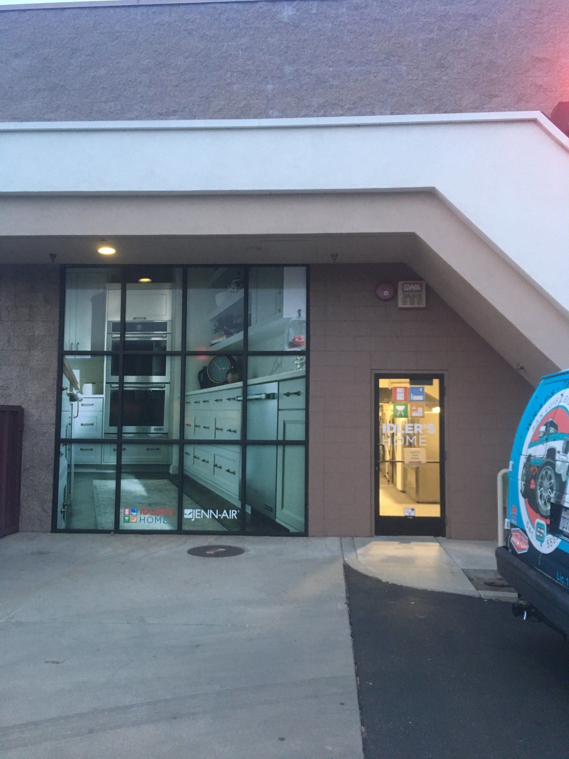 Storefront entrance with glass windows and a lit doorway beside a parked vehicle at dusk