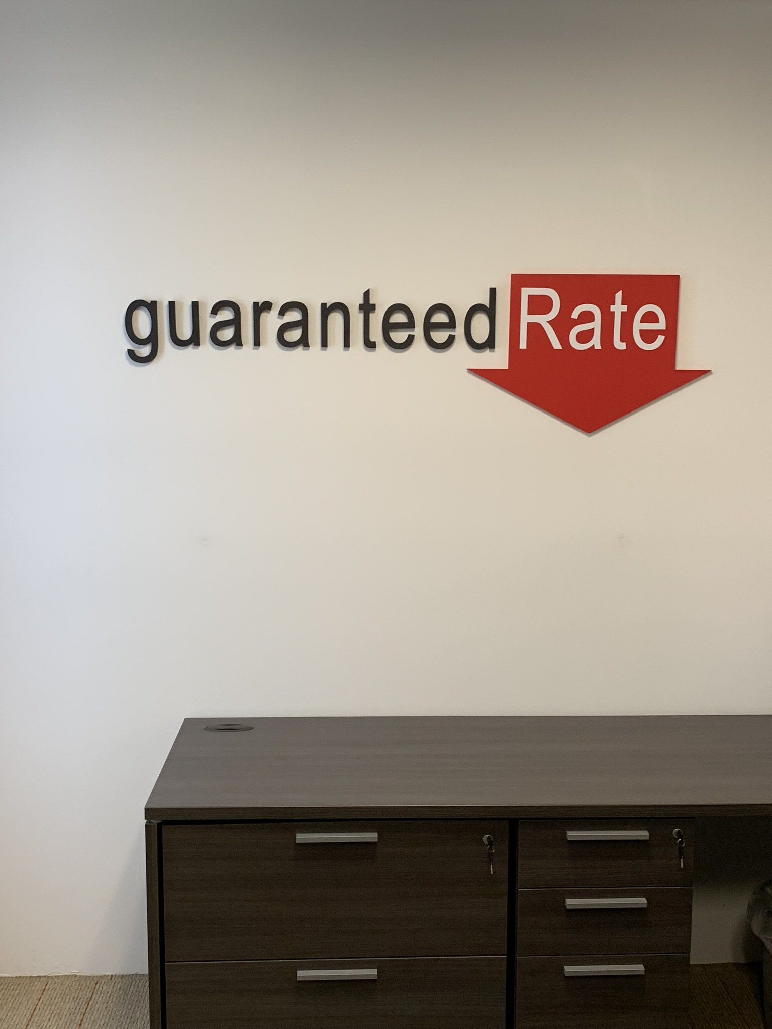 Wall sign reading “guaranteed Rate” with a red downward arrow above a dark cabinet