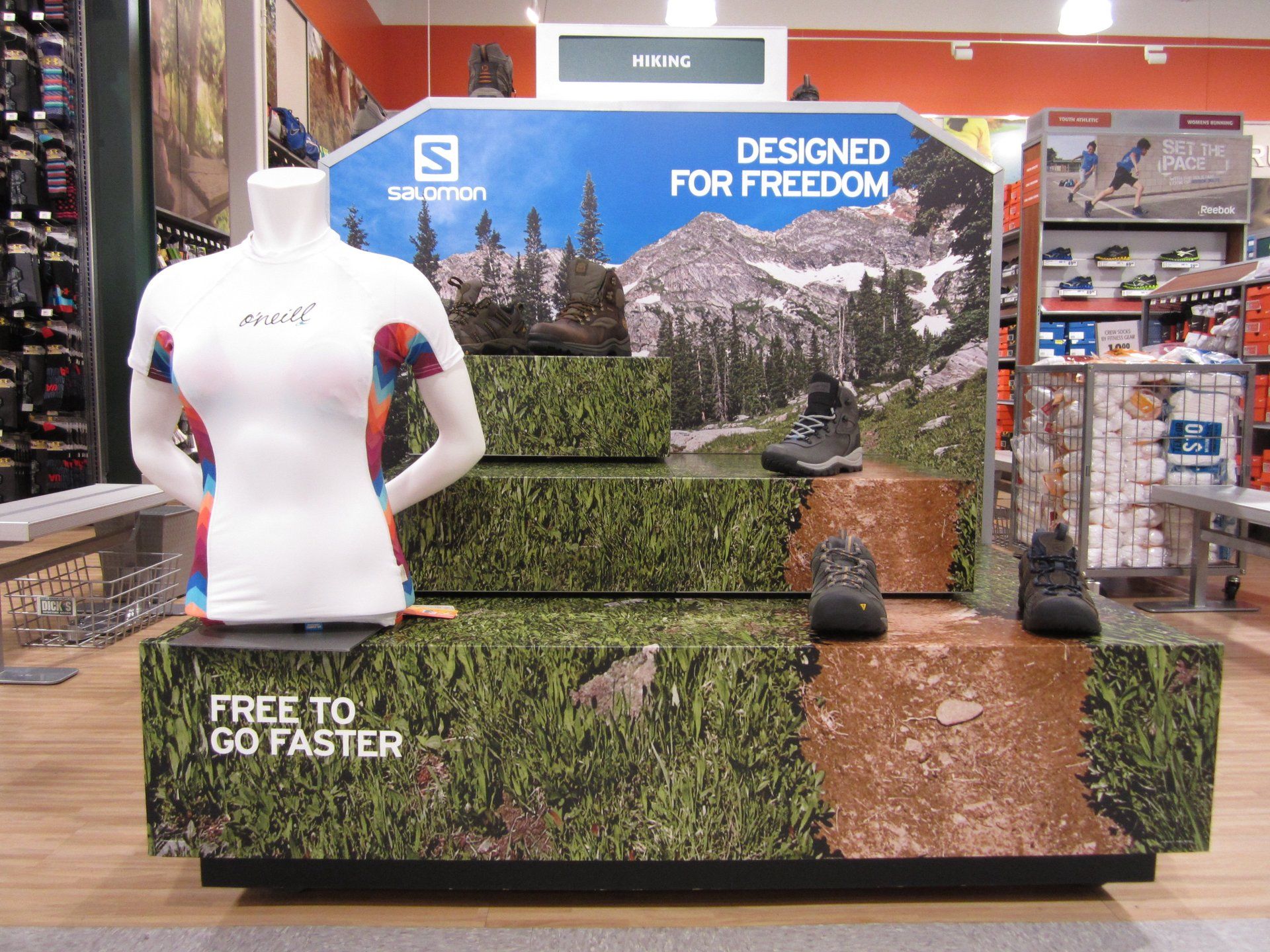 Store display with white mannequin, mountain backdrop, and signs reading “Designed for Freedom” and “Free to Go Faster”