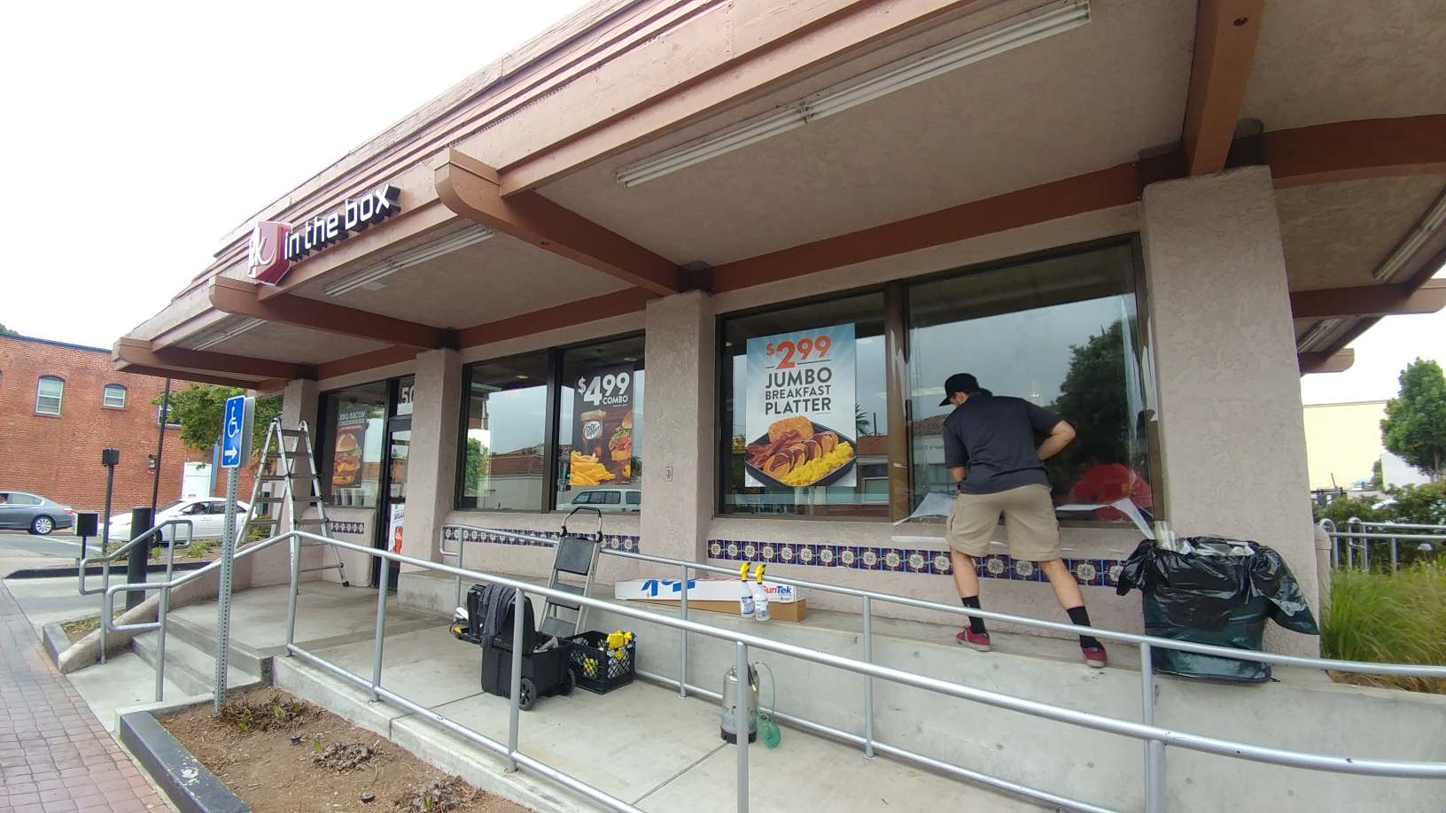 Person arranging items outside a storefront with windows and a ramp, likely after a cleanup or delivery.
