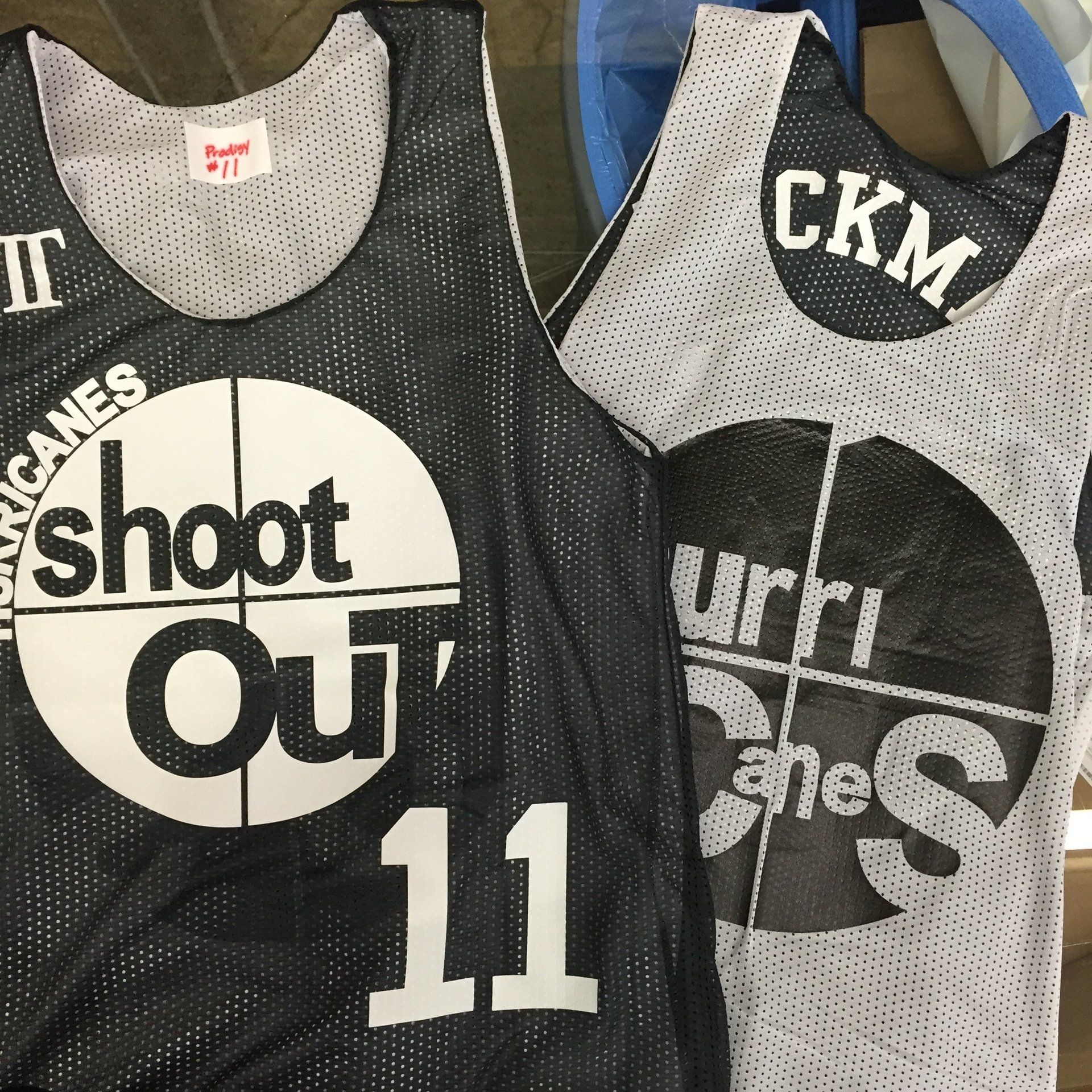 Two basketball jerseys hanging side by side, black and gray with large white team text and numbers.