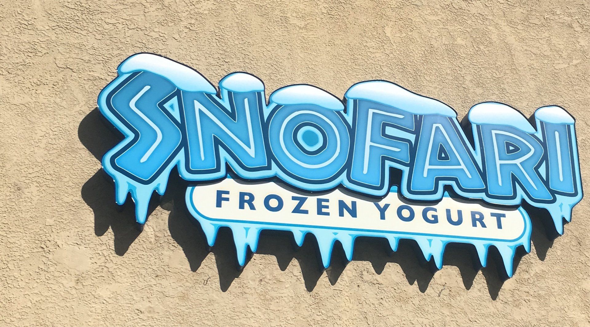Blue SnoFari Frozen Yogurt sign on a beige stucco wall