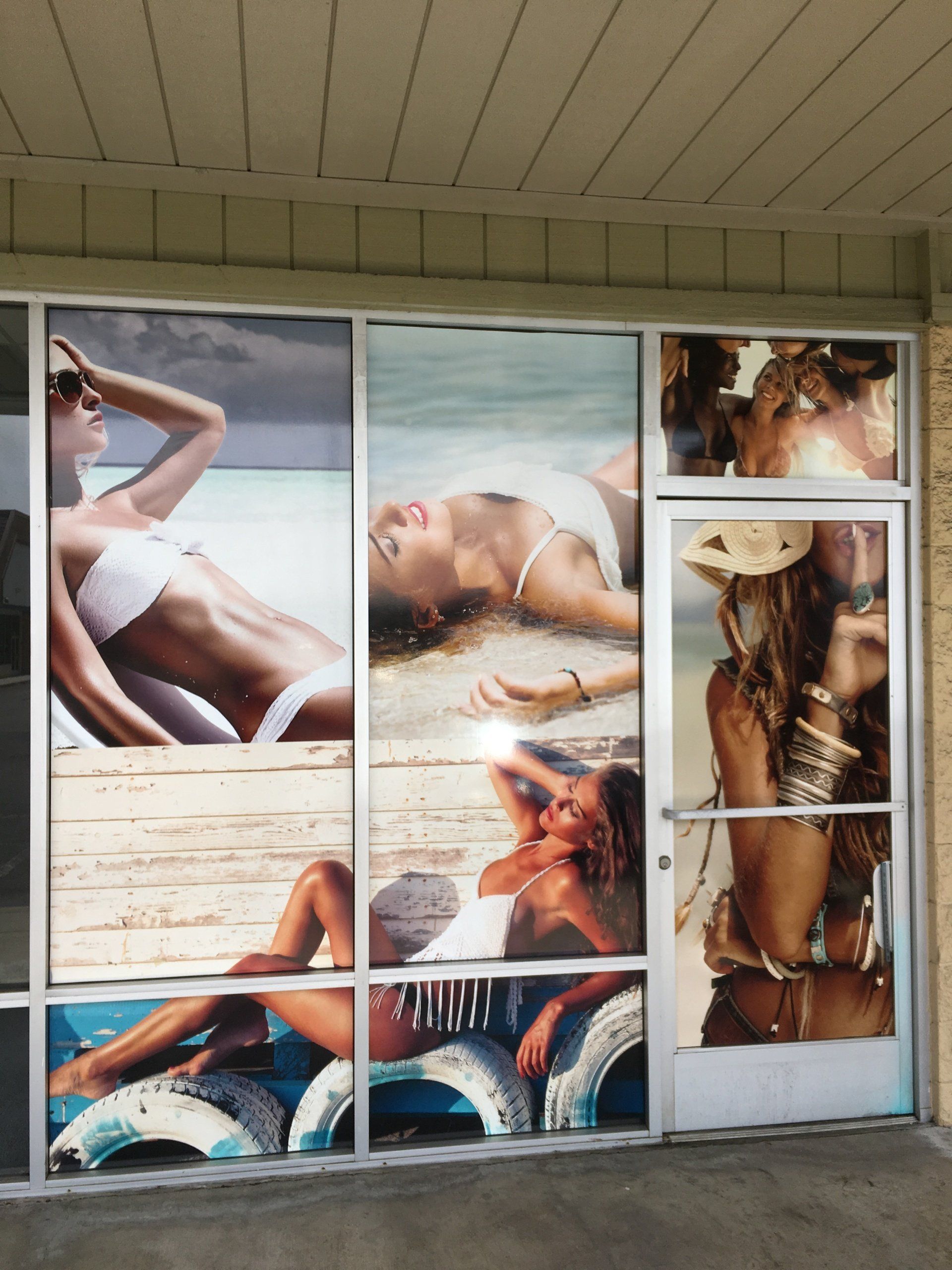 Beach-themed wall display with multiple beachwear posters in blue, tan, and white tones